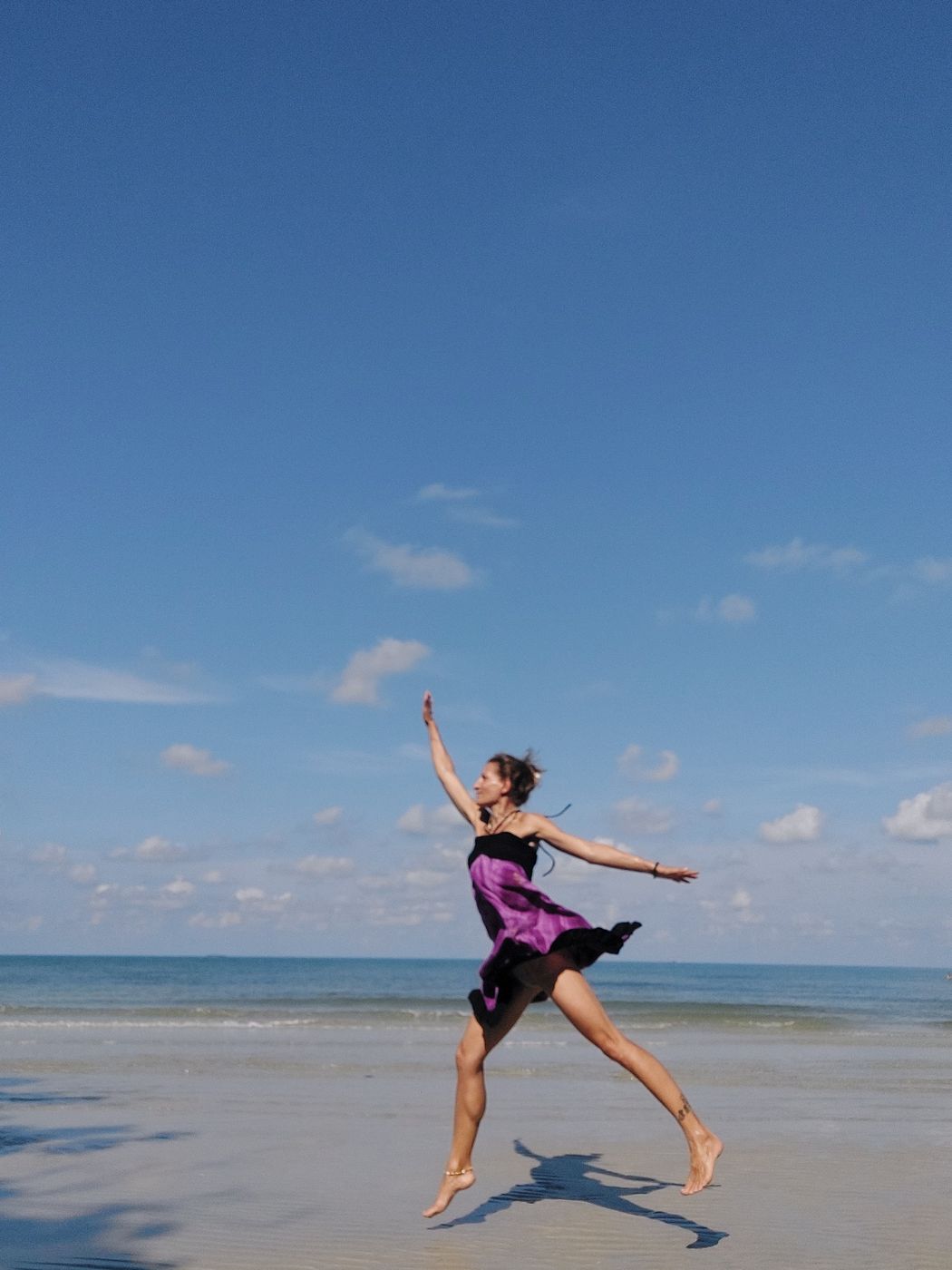 Alice springt tanzend über den Strand, ein violettes Kleid weht im Wind