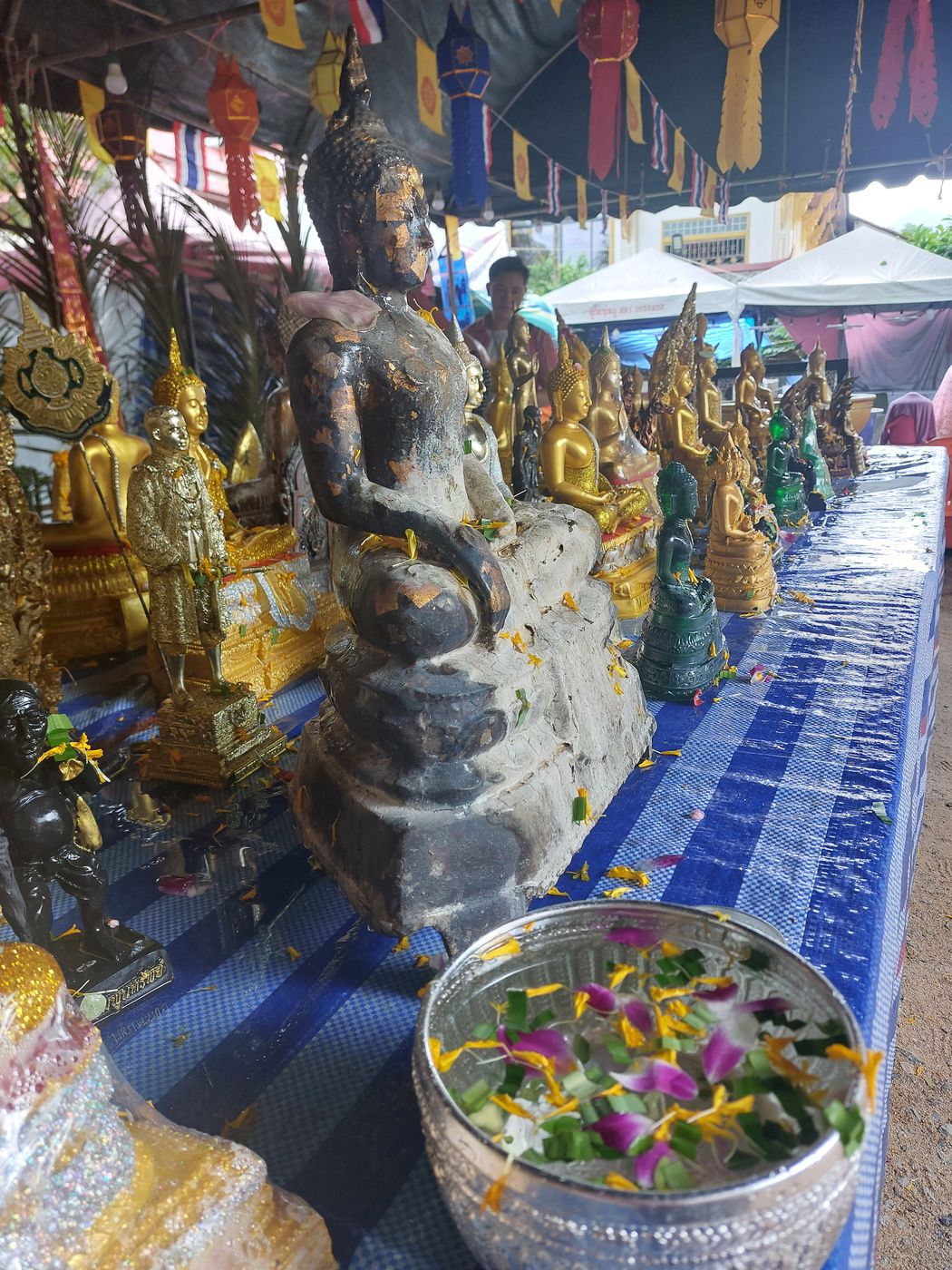 Buddha-Statuen mit Blütenblättern und einer Silberschale mit Blüten beim Songkran-Fest
