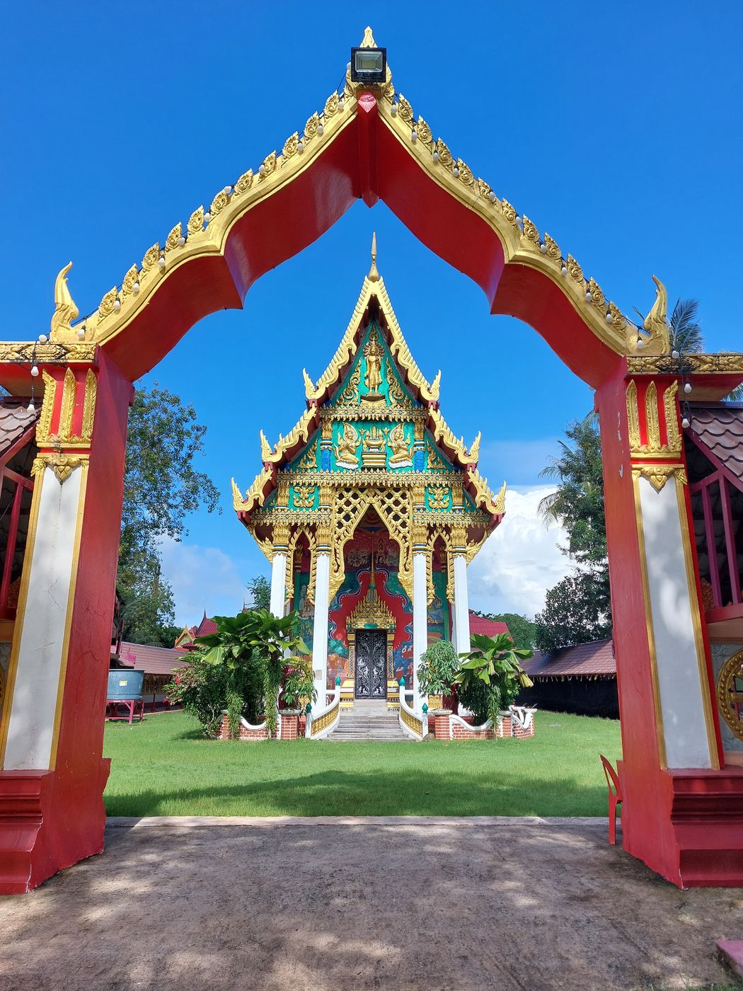Buddhistischer Tempel hinter einem rot-goldenen Eingangstor unter blauem Himmel